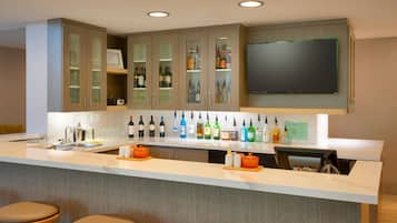 A modern kitchen with a bar area, featuring a wine and liquor display, a large flat-screen TV, and bar stools.