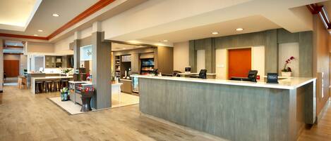 Una moderna area reception di un hotel con un banco centrale, zona bar e un minibar ben visibile.