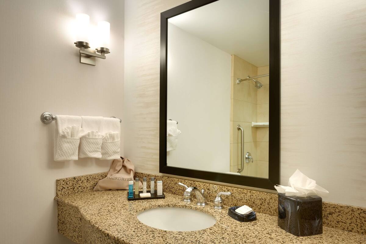 A bathroom with a sink, mirror, towel rack, and toiletries.