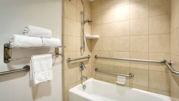 Un baño con una bañera blanca, barras de apoyo, un perchero con toallas dobladas y un cabezal de ducha.