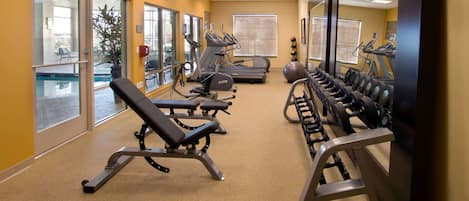 Ett gym med träningsutrustning, en stor spegel och ett fönster med utsikt över omgivningen.