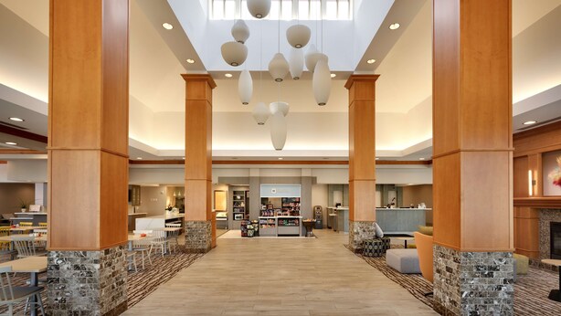A spacious lobby with high ceilings, wooden pillars, and hanging pendant lights. - Hilton Garden Inn Salt Lake City/Sandy (Sandy)