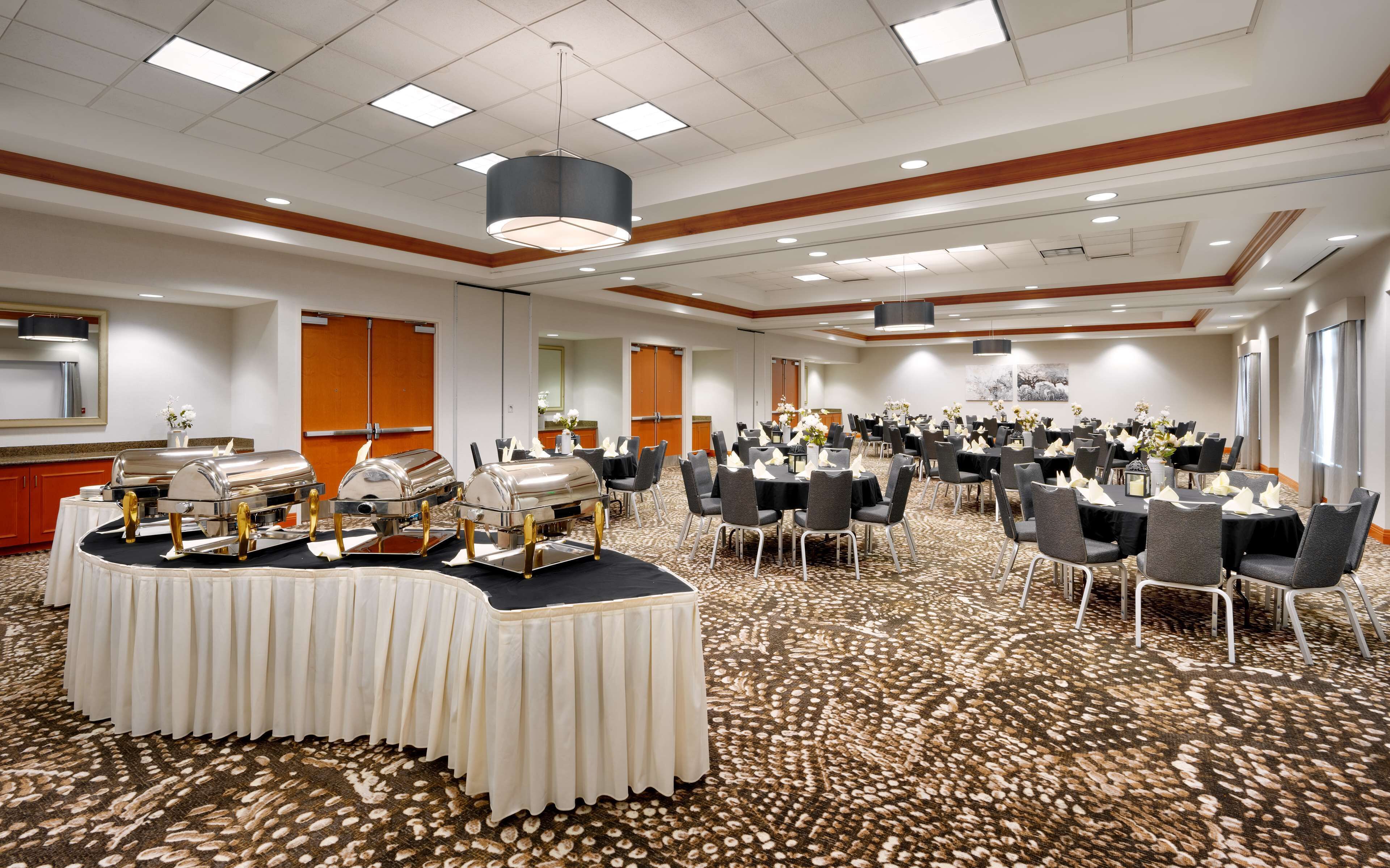 Een ruime congreszaal met ronde tafels, stoelen en een buffetopstelling.