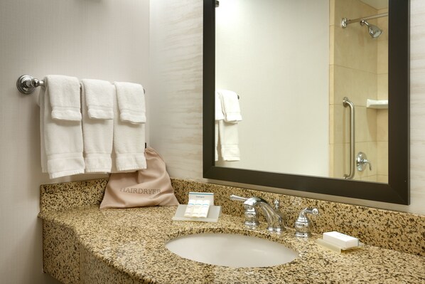 Une salle de bain avec un lavabo doté d’un plan de travail en granit, un miroir et un porte-serviettes avec trois serviettes.