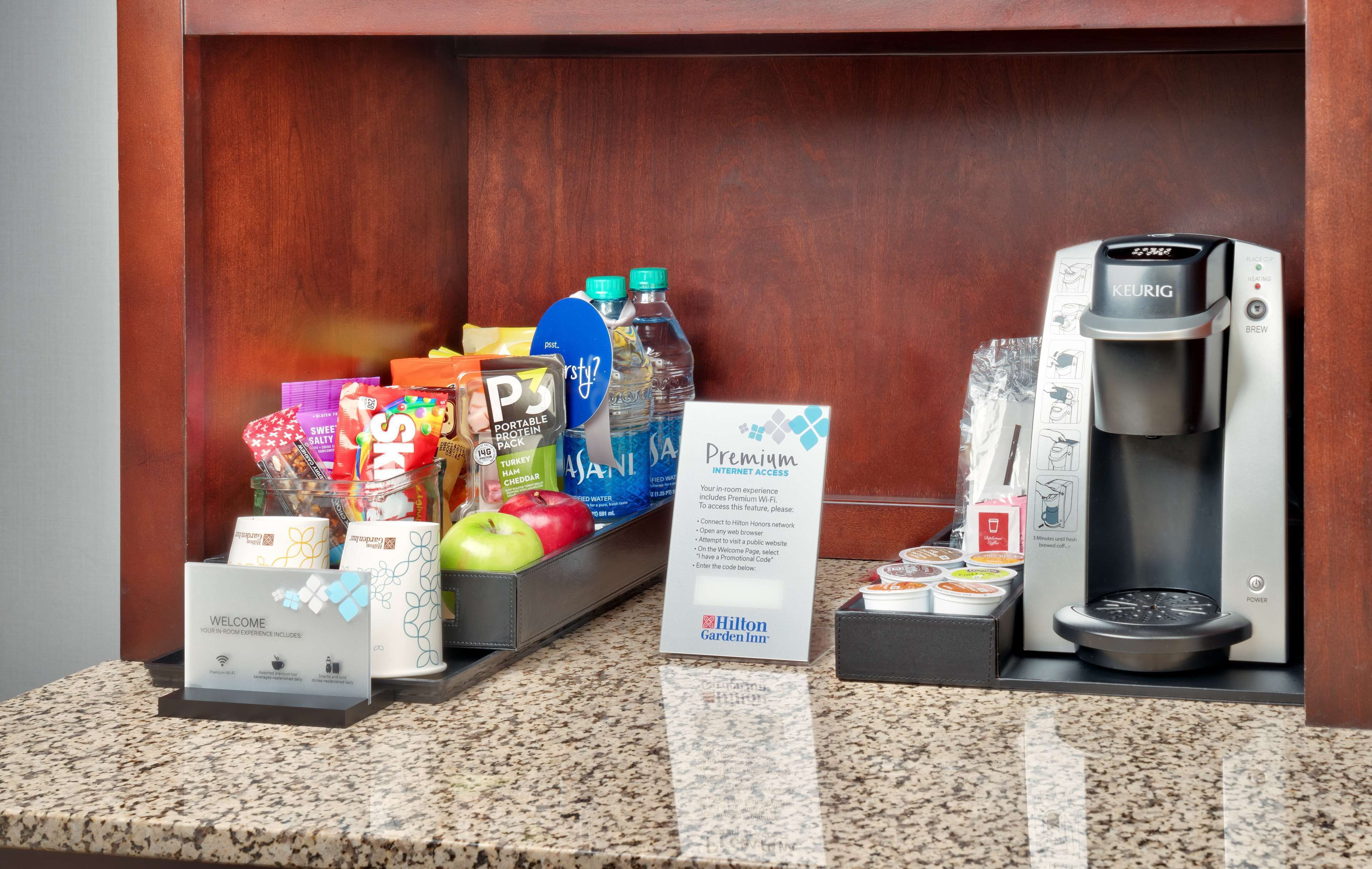 Zona de recepción de hotel con una máquina de café, un cartel de bienvenida y diferentes alimentos y bebidas.