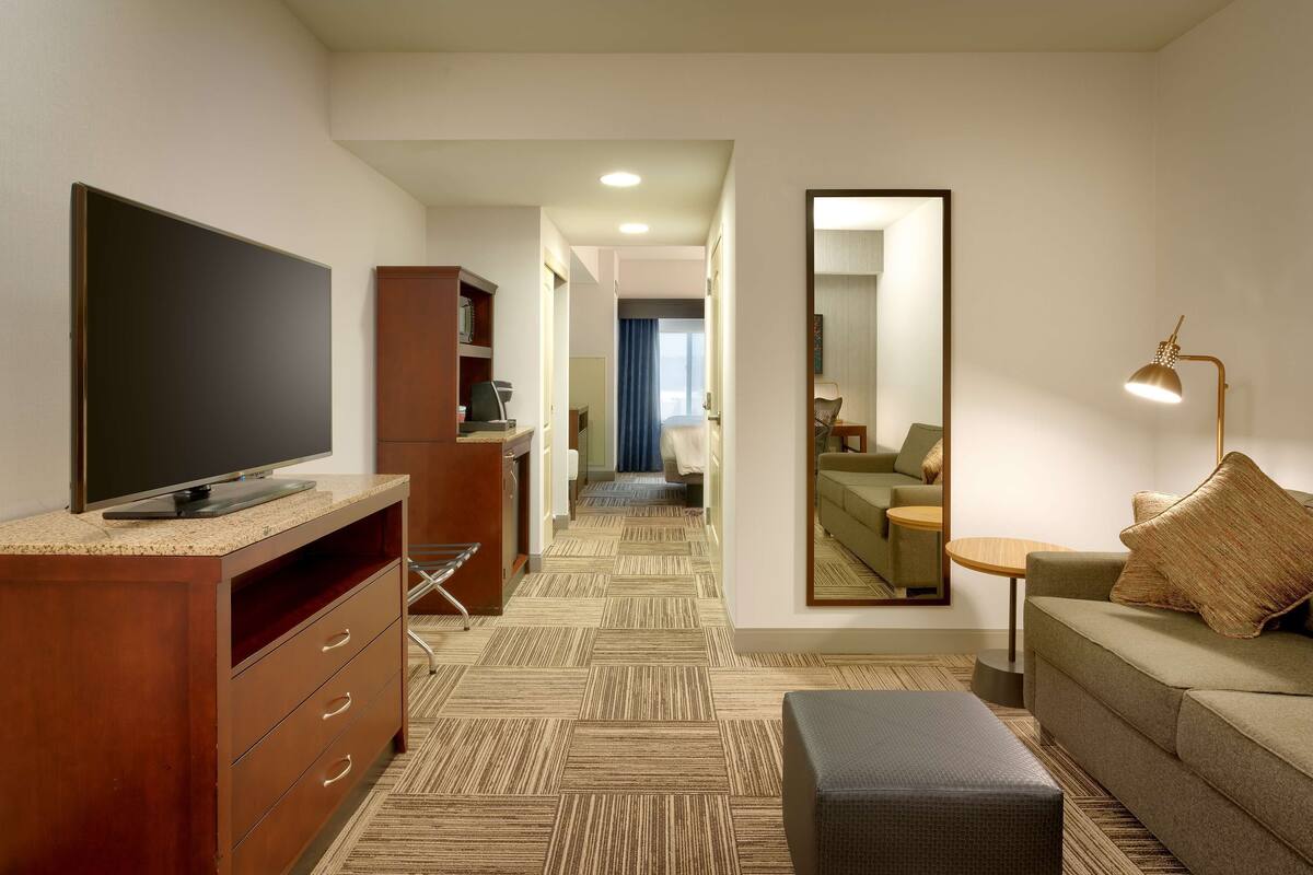 A hotel room with a television, a desk, a mirror, a sofa, and a lamp.