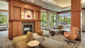 A spacious lobby with a fireplace, comfortable seating, large windows, and a view of the outdoors. - Hilton Garden Inn Salt Lake City/Sandy (Sandy)