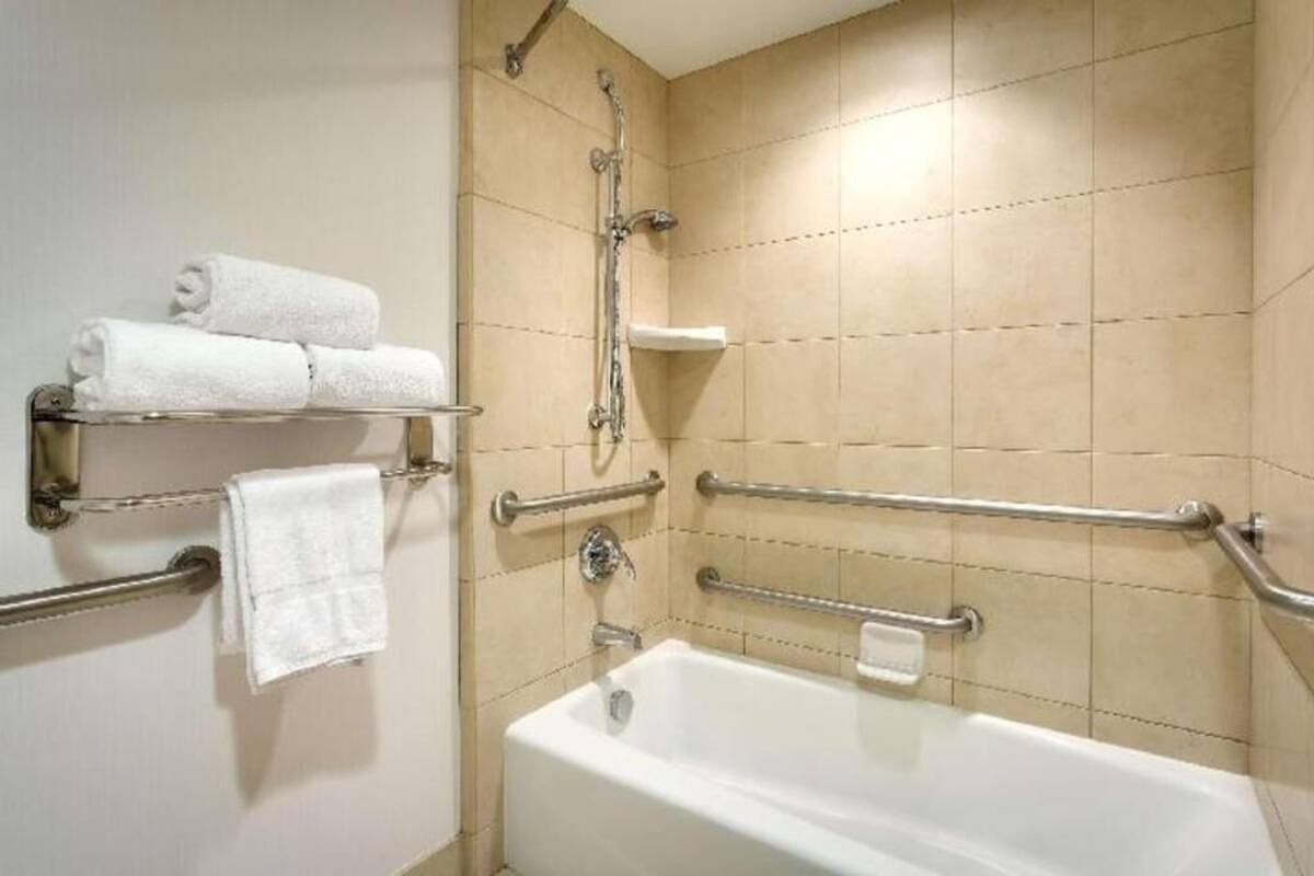 A bathroom with a bathtub, handrails, a showerhead, and a towel rack with towels.