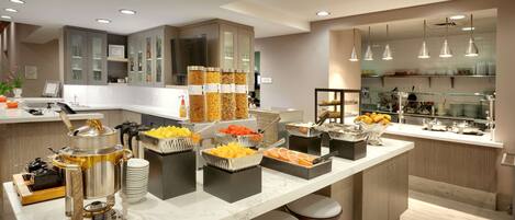 A modern kitchen with a marble countertop, various food stations, and a coffee machine.