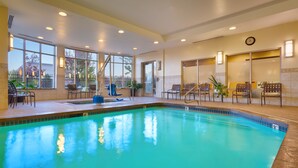 An indoor swimming pool with clear blue water, surrounded by seating areas with chairs and tables, and large windows providing natural light. - Hilton Garden Inn Salt Lake City/Sandy (Sandy)