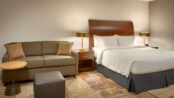 A hotel room with a bed, a sofa, a nightstand, and a lamp.