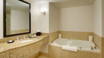 Un baño con encimera de granito, dos lavamanos, un espejo grande, una lámpara empotrada en la pared, una bañera y un perchero.