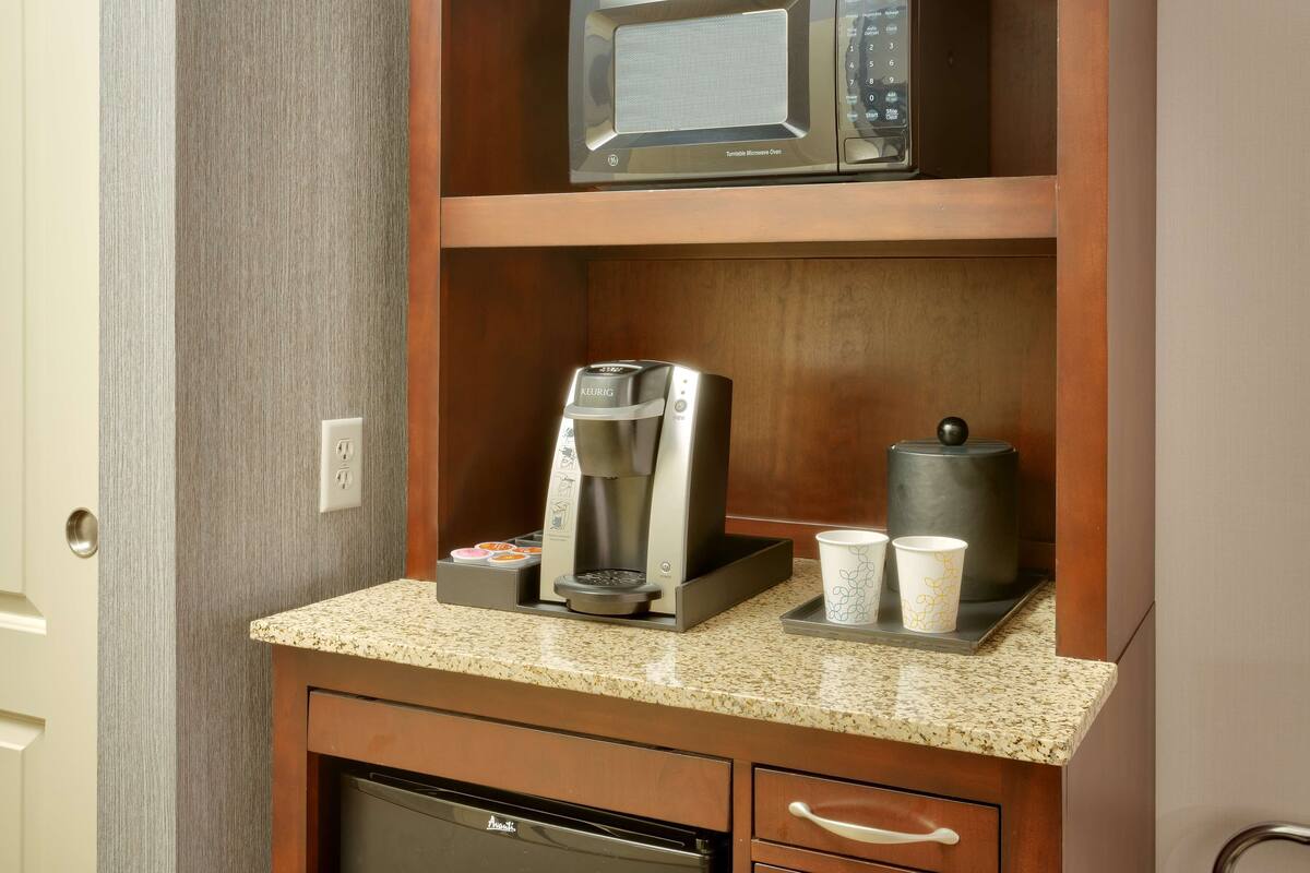 A kitchenette with a microwave, coffee maker, and cups on the counter.