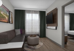 Una habitación de hotel moderna con sofá, reposapiés, televisor de pantalla plana y obras de arte en las paredes.