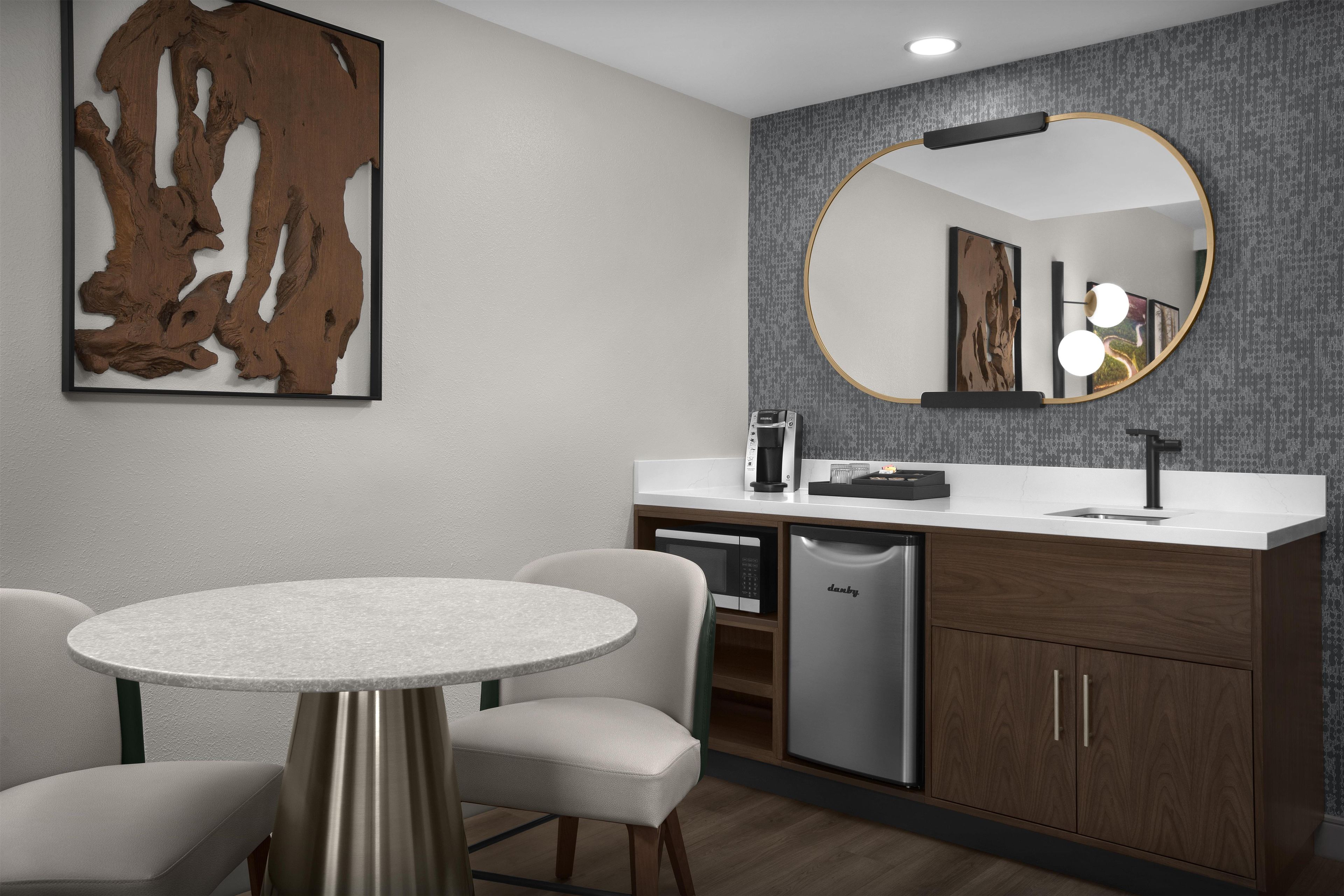 A modern bathroom with a round mirror, a sink, a coffee maker, and a dishwasher.