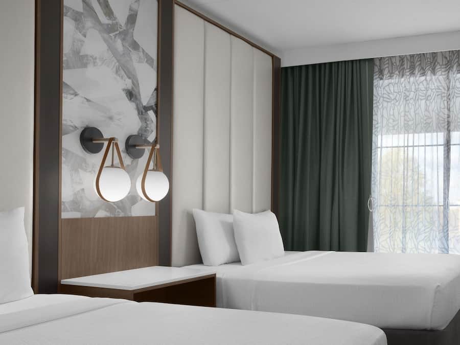 Habitació d'hotel amb dos llits, una paret de marbre, un panell de fusta al capçal i una finestra amb cortines.