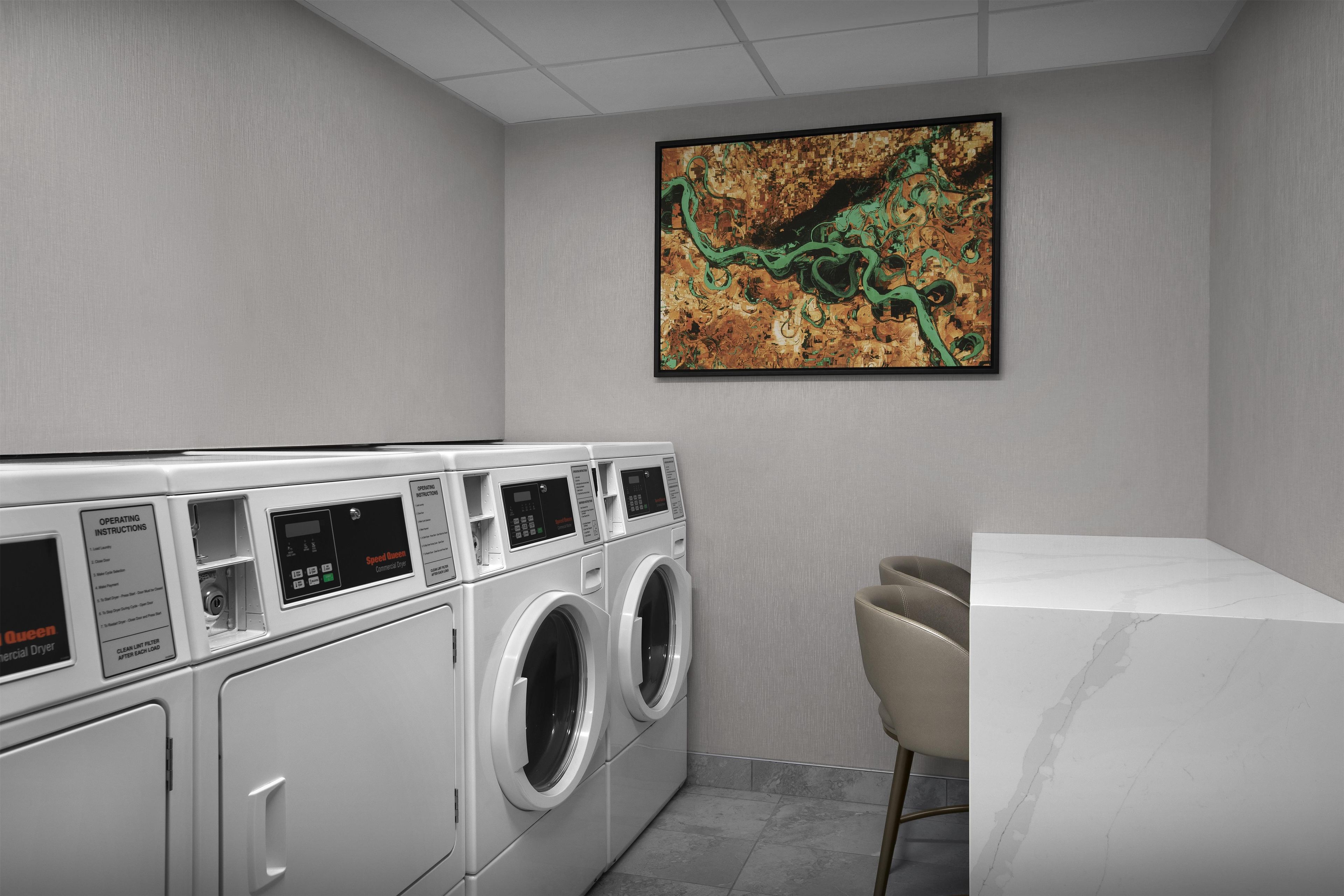 A laundry room with a commercial dryer, a wall-mounted painting, and a seating area.