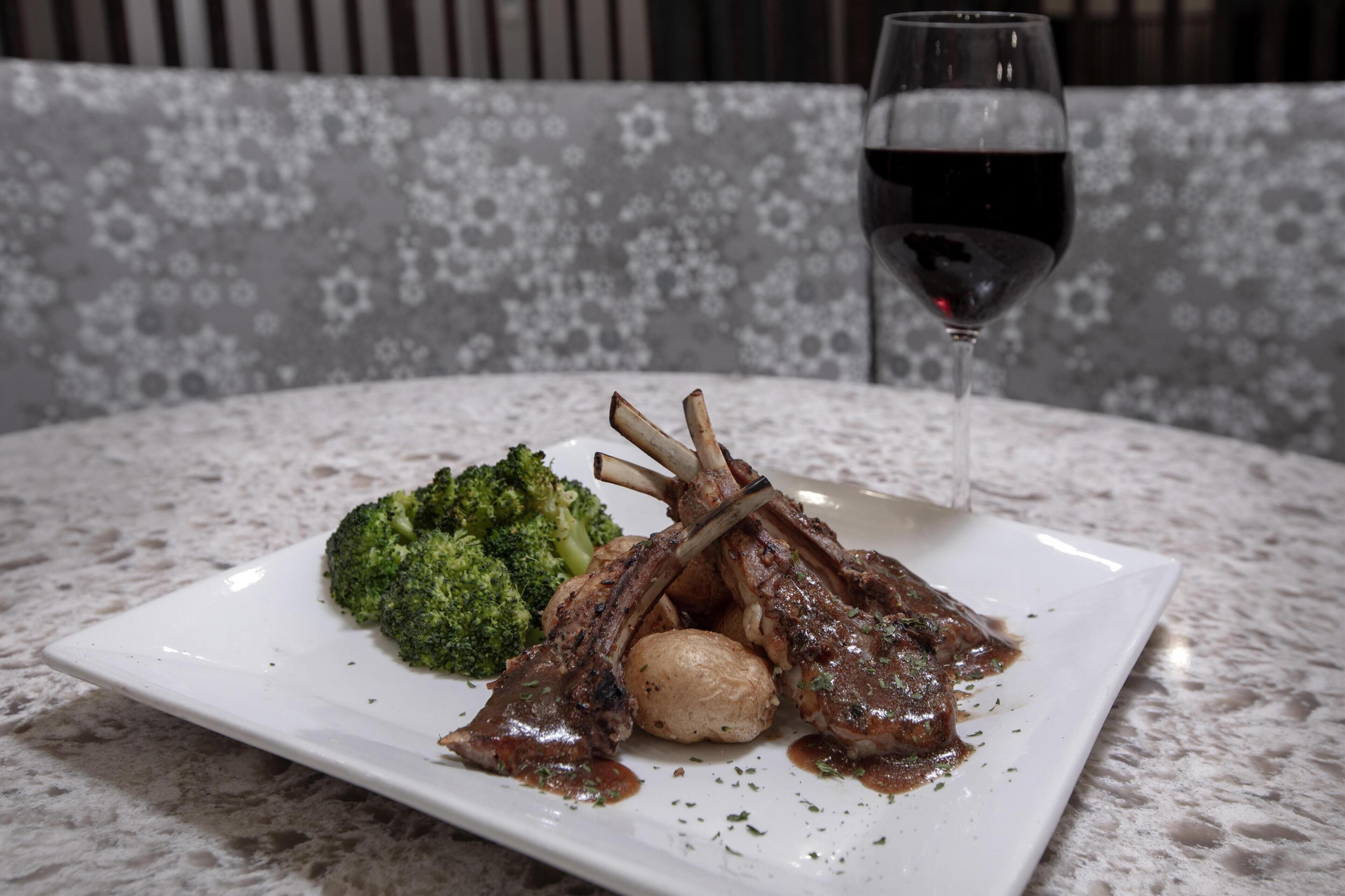 A plate with lamb chops, broccoli, and a glass of red wine on a marble table.