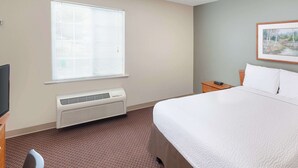 A hotel room with a bed, a window with blinds, a heater, a nightstand, and a painting on the wall. - WoodSpring Suites Sioux Falls (Sioux Falls)