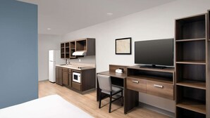 A compact hotel room with a kitchenette, a bed, a desk, and a TV. - WoodSpring Suites Holland - Grand Rapids (Holland)