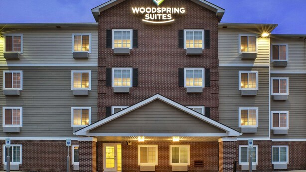 A hotel with a prominent "Woodspring Suites" sign, multiple windows, and a brick facade. - WoodSpring Suites Holland - Grand Rapids (Holland)