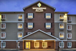 A hotel with a prominent "Woodspring Suites" sign, multiple windows, and a brick facade. - WoodSpring Suites Holland - Grand Rapids (Holland)