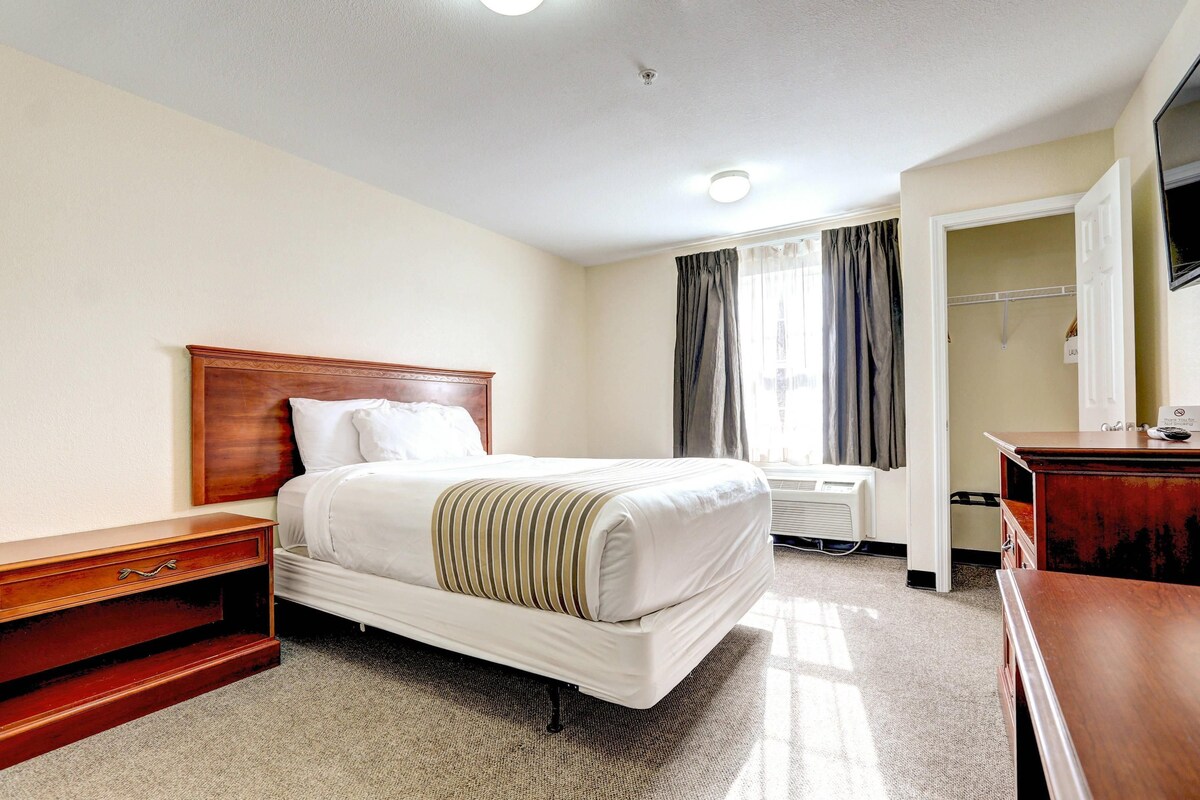 A hotel room with a bed, bedside table, a desk, a chair, a radiator, and a wardrobe.