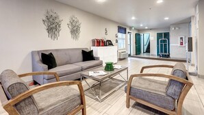 En moderne stue med en grå sofa, træstole, et glasbord og dekorativ vægkunst.
