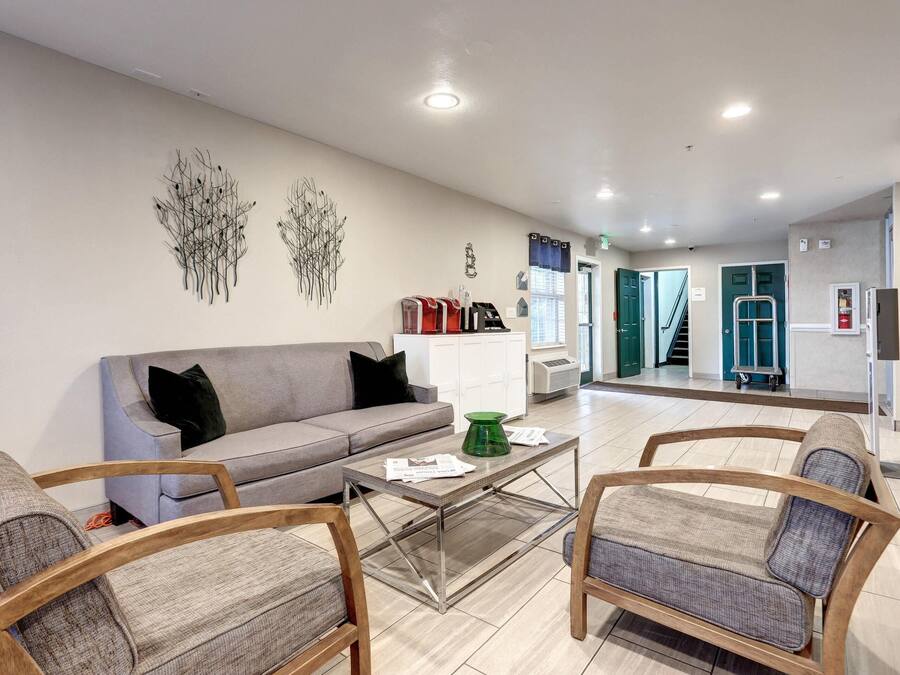 Una sala de estar moderna con un sofá gris, sillas de madera, una mesa de centro de vidrio y decoración en la pared.