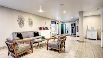 A spacious lobby with a grey sofa, two wooden chairs, a coffee table, and a decorative wall piece.