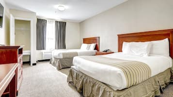 A hotel room with two beds, a desk, a wardrobe, and a window with curtains.