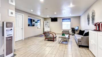 A clean, well-lit reception area with a hand sanitizer dispenser, a seating area with a sofa and chairs, and a television mounted on the wall.