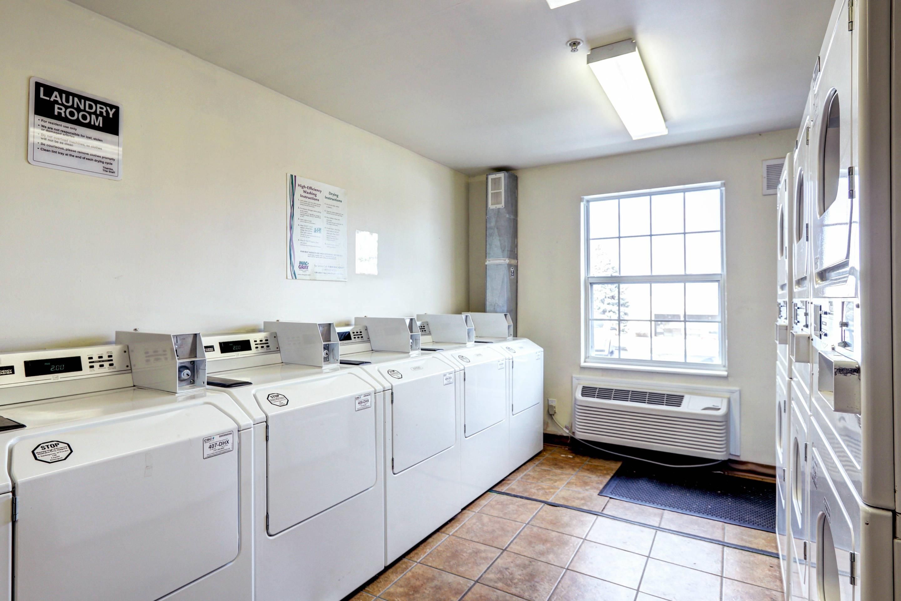 A laundry room with multiple washing machines and dryers, a sign indicating it is for resident use, and a window providing natural light.