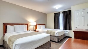 Et hotelværelse med to senge, et skrivebord, en lampe og et vindue med gardiner.