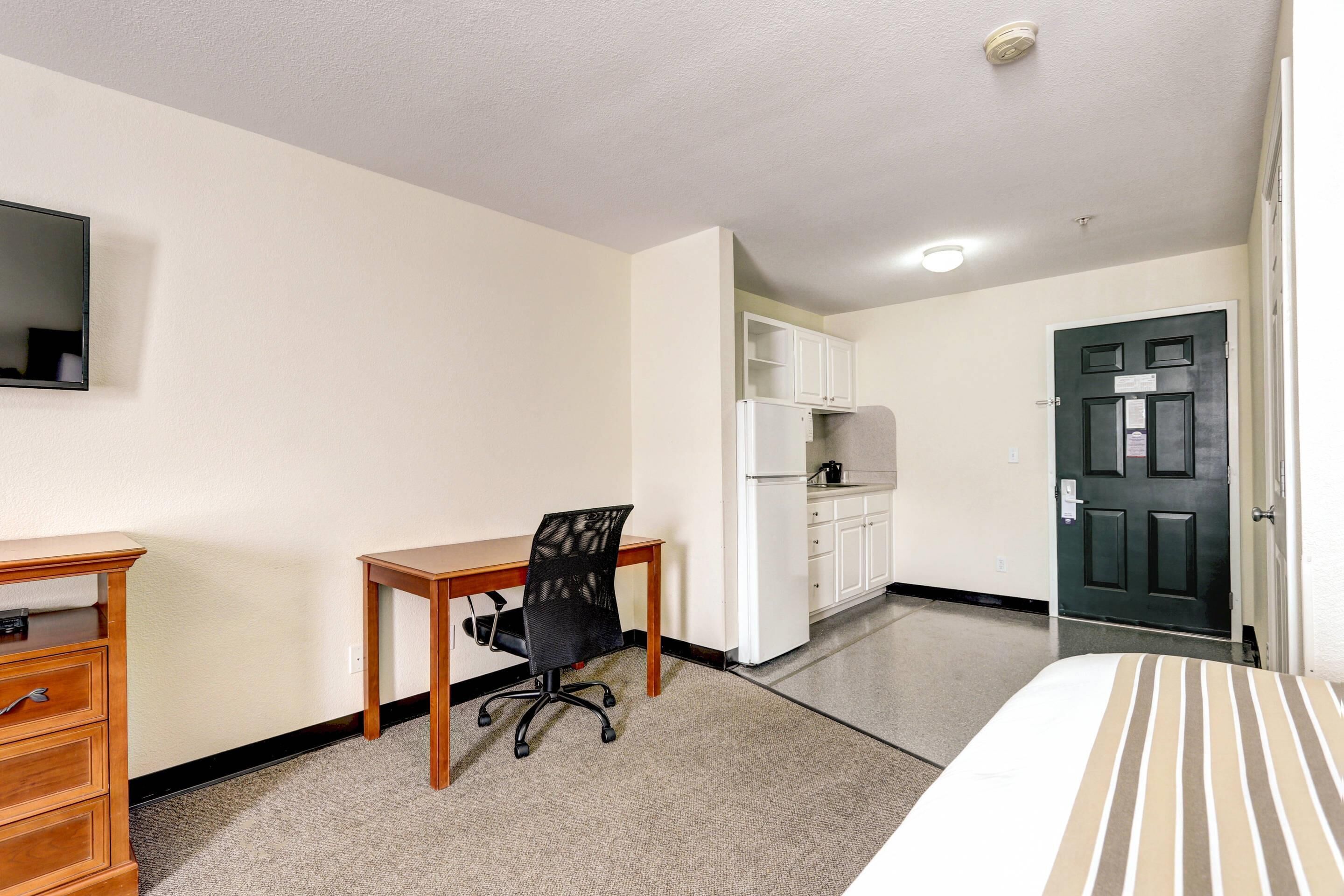 A hotel room with a bed, a desk with a chair, a television, a wardrobe, and a door.