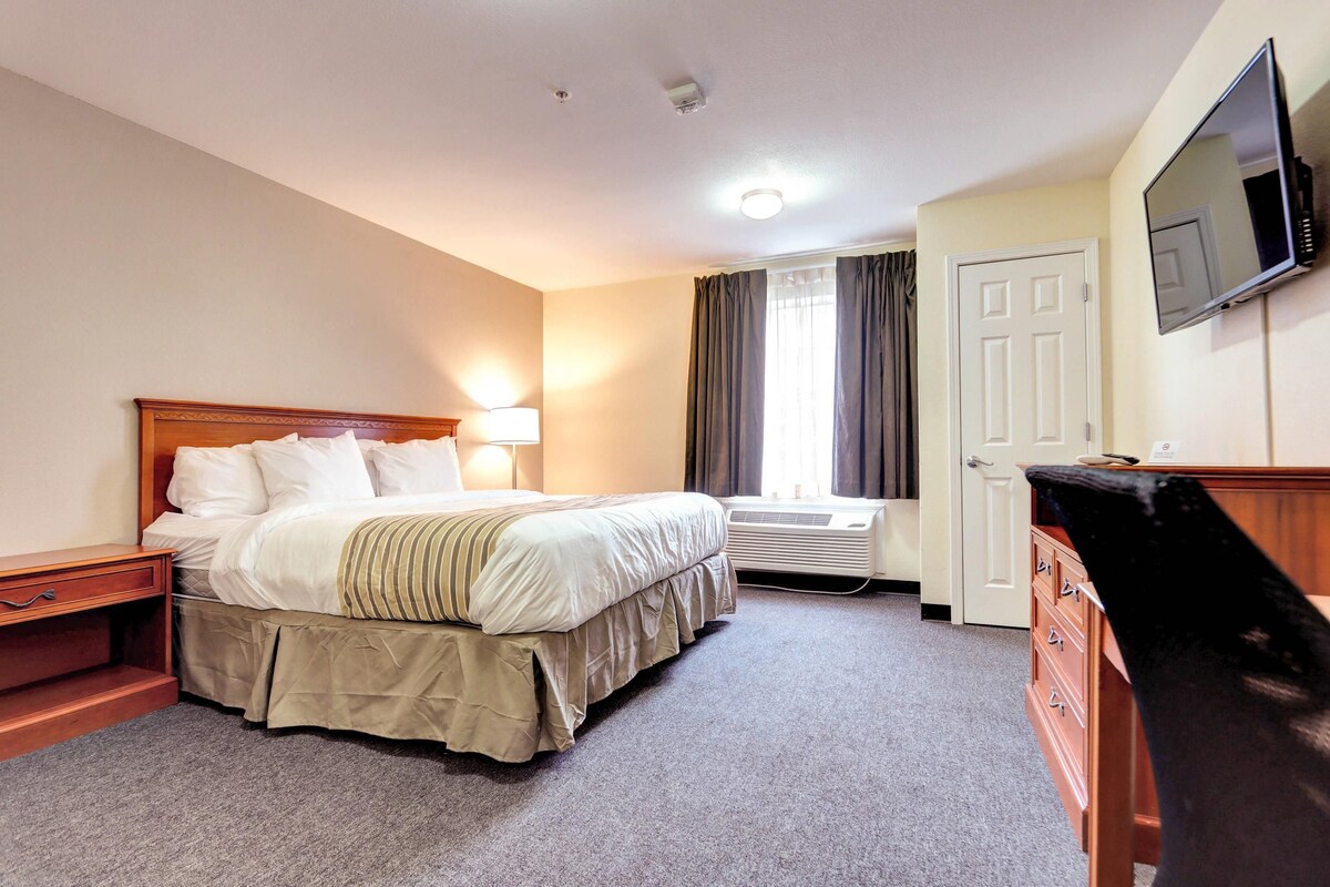 A hotel room with a bed, bedside table, lamp, air conditioning unit, television, and a door.