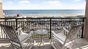 A balcony with two white Adirondack chairs and a small round table, overlooking a beach and parking area. - Tilghman Beach And Golf Resort (North Myrtle Beach)