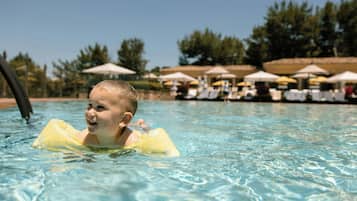 A child in a pool with clear water, surrounded by lounge chairs and umbrellas.