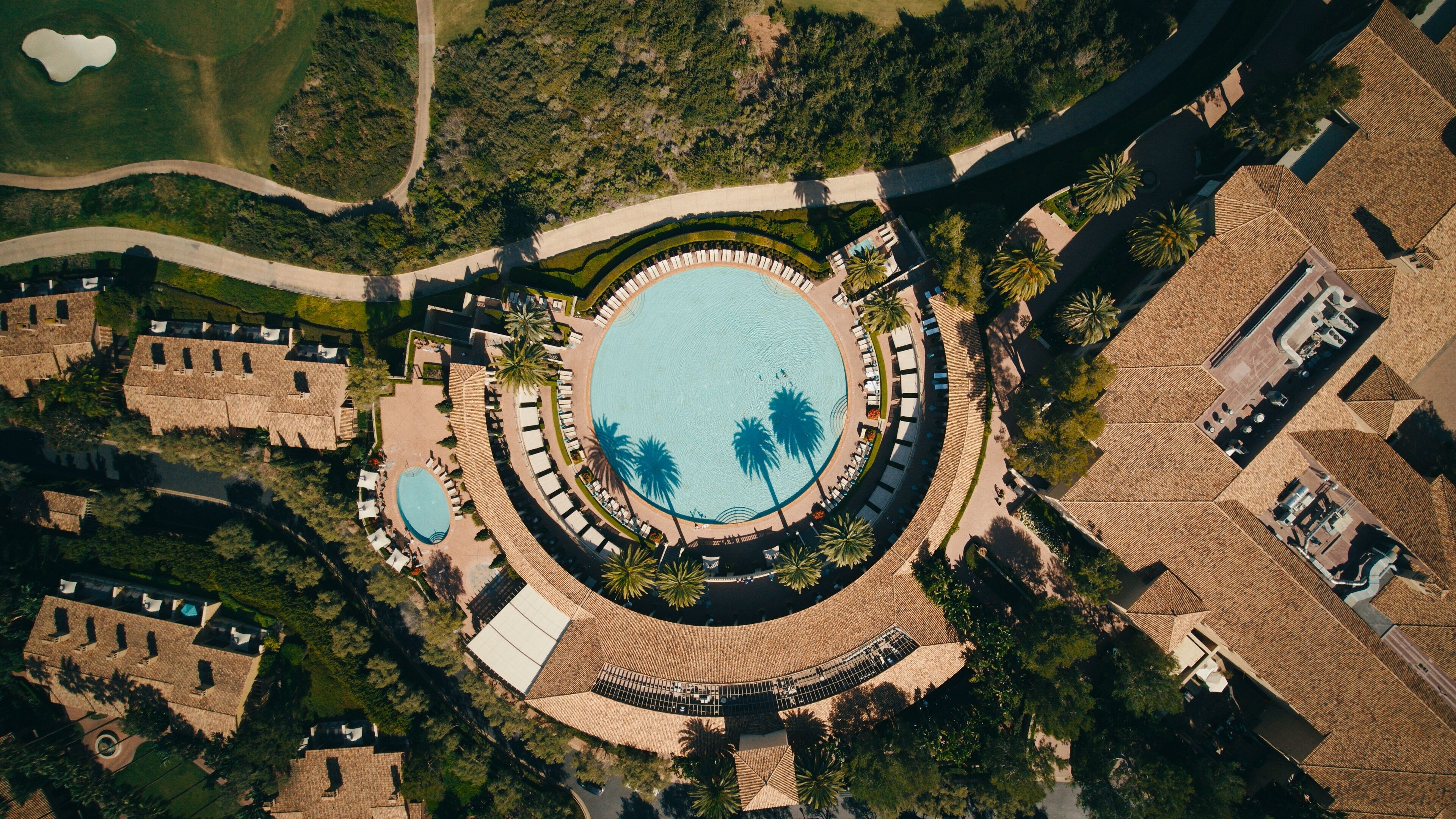 Vue aérienne d’un complexe hôtelier doté d’une piscine centrale, de plusieurs villas pour les clients et de palmiers.