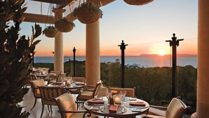 A restaurant with round tables and chairs, large windows, and hanging plants. - The Resort at Pelican Hill (Newport Beach)