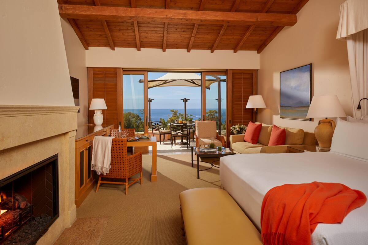 Ein Hotelzimmer mit Kamin, einer Couch, einem Bett, einem Essbereich mit Tisch und Stühlen sowie Meerblick.