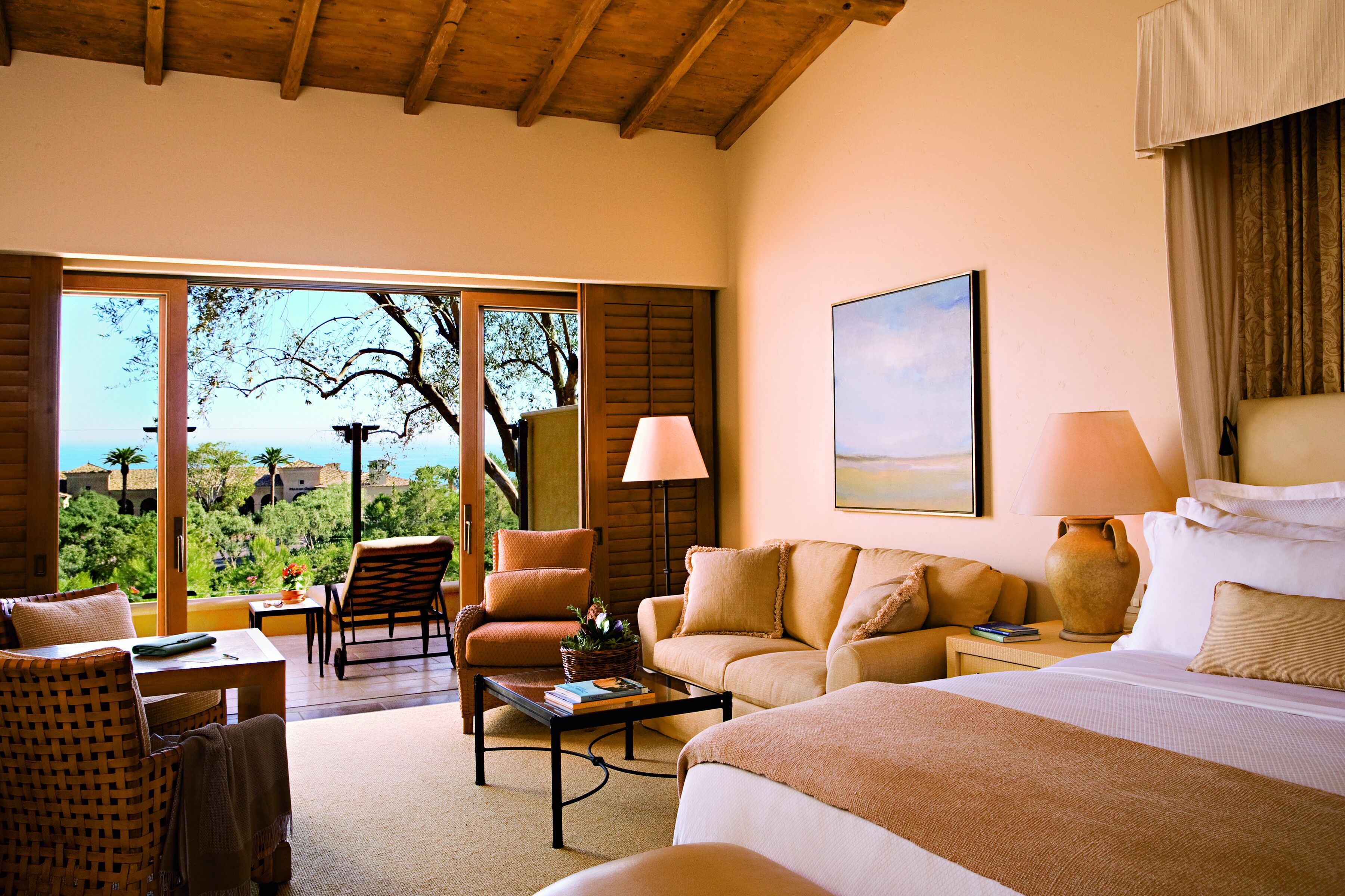 Quarto de hotel com cama, sofá, cadeira, mesa e vista para o exterior.