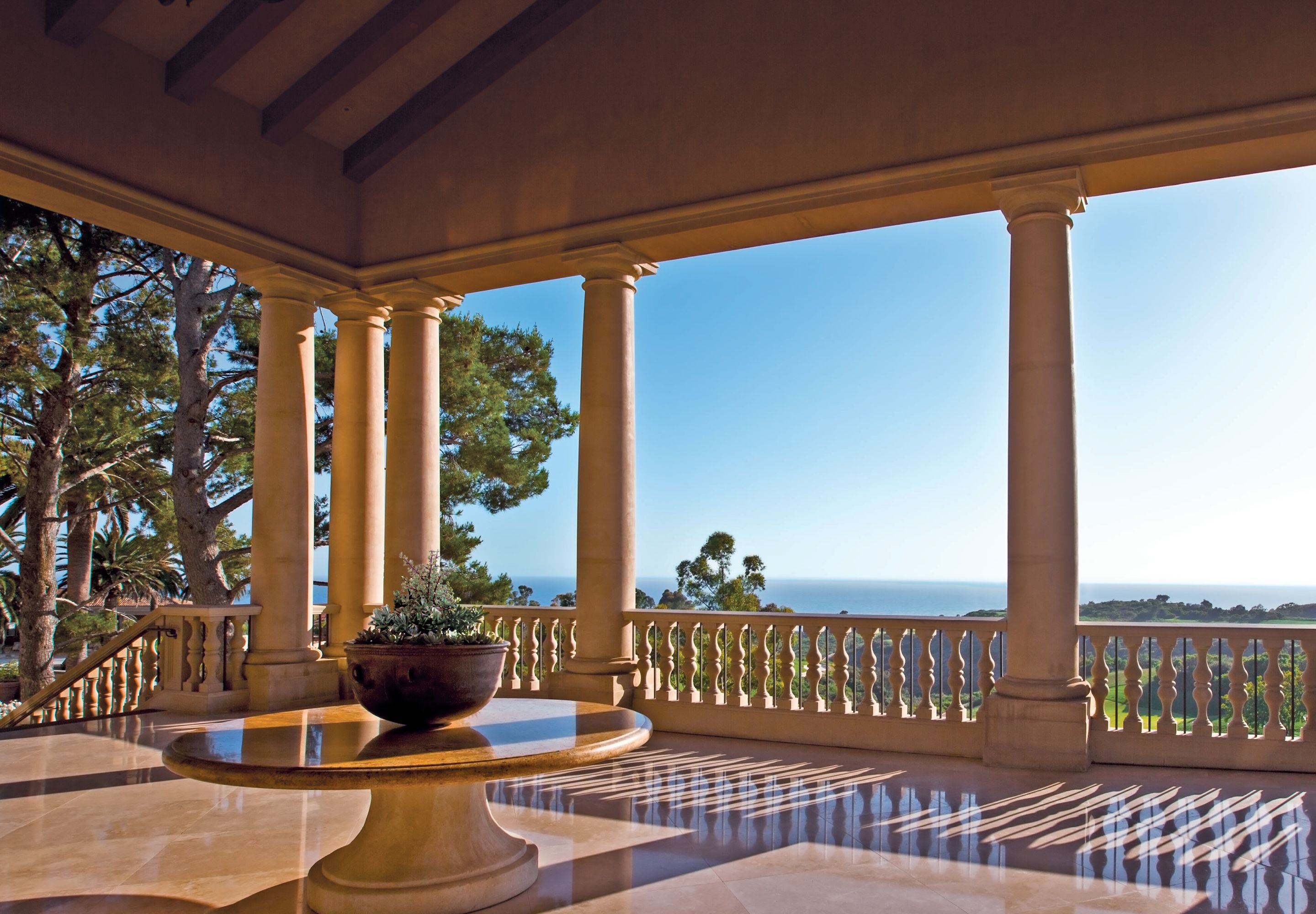 Un espacio al aire libre techado con columnas, una planta en maceta y vistas al mar.