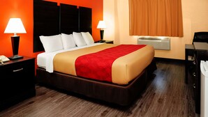 A hotel room with a large bed, two bedside lamps, a nightstand, a desk, and a window with curtains.