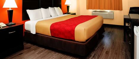 A hotel room with a large bed, two bedside lamps, a nightstand, a desk, and a window with curtains.