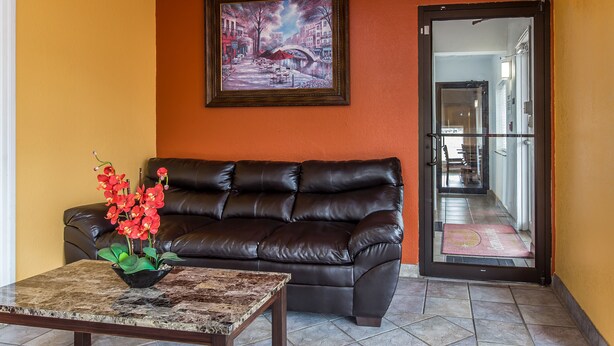 A living room with a dark leather sofa, a coffee table with a vase of red flowers, and a framed painting on the wall.