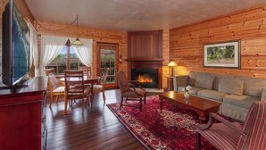 Interior de una cabaña de troncos con chimenea, muebles de madera y un comedor.