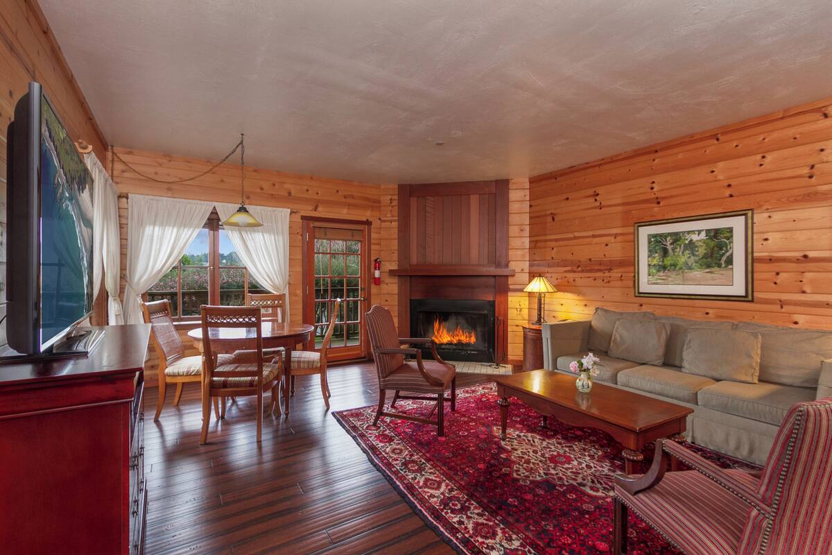 A log cabin interior with a fireplace, wooden furniture, and a dining area.