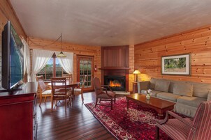 Interior de una cabaña de troncos con chimenea, muebles de madera y un comedor.