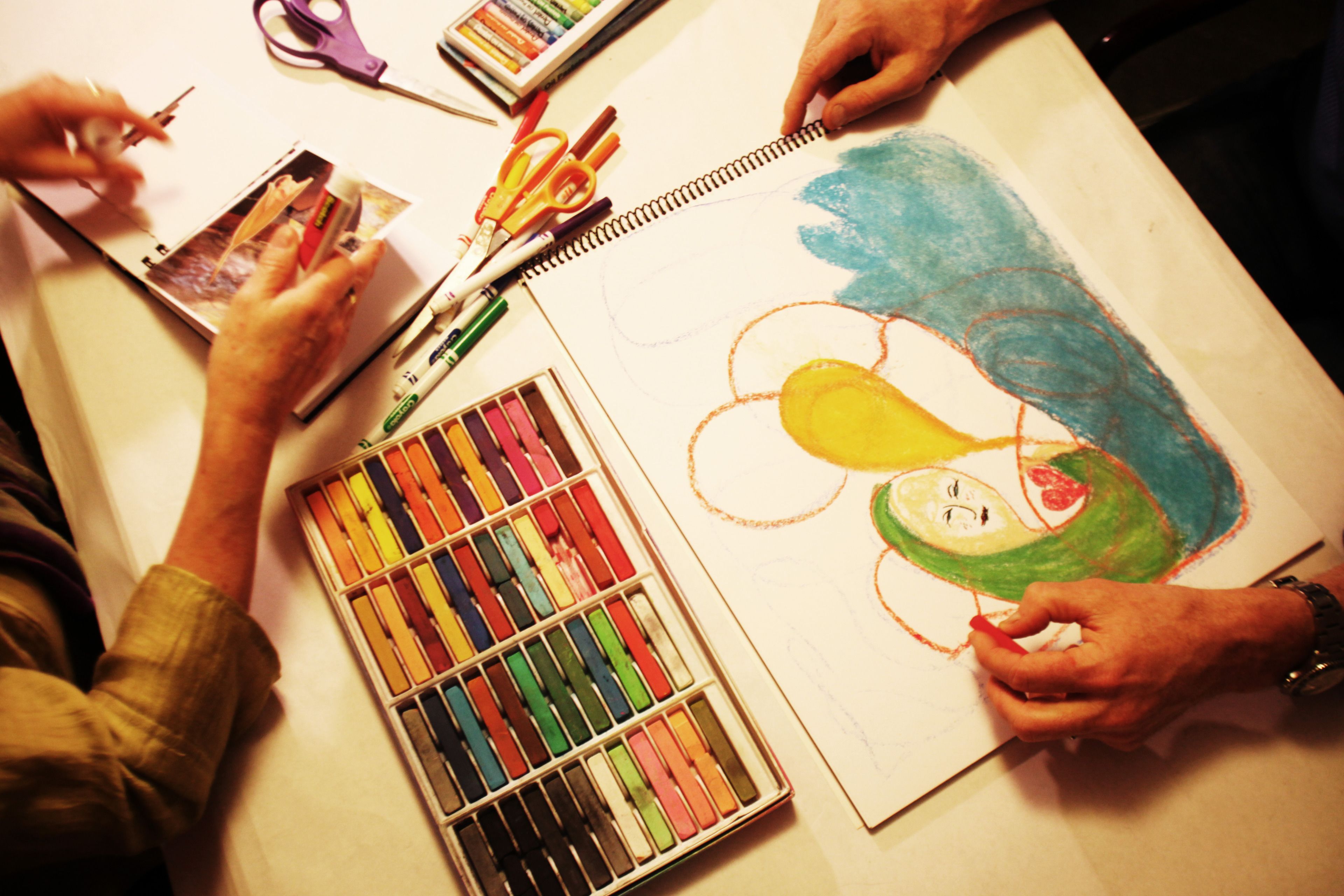 Una persona dibujando en un bloc de dibujo con lápices de colores y rotuladores.